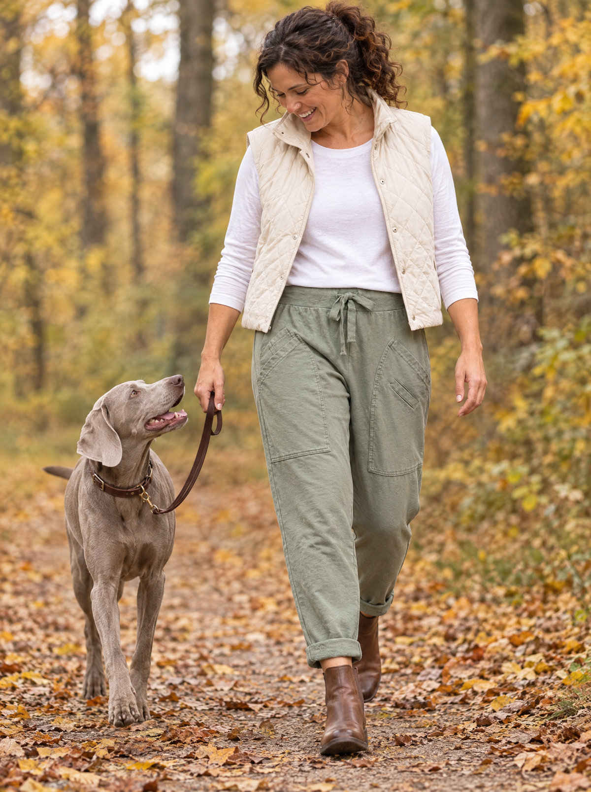 Frau in der Glückshose in Khaki geht mit ihrem Weimaraner durch den Herbstwald